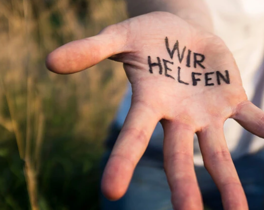 Eine offene Hand mit dem Schriftzug 'WIR HELFEN', die Unterstützung und Hilfe symbolisiert.