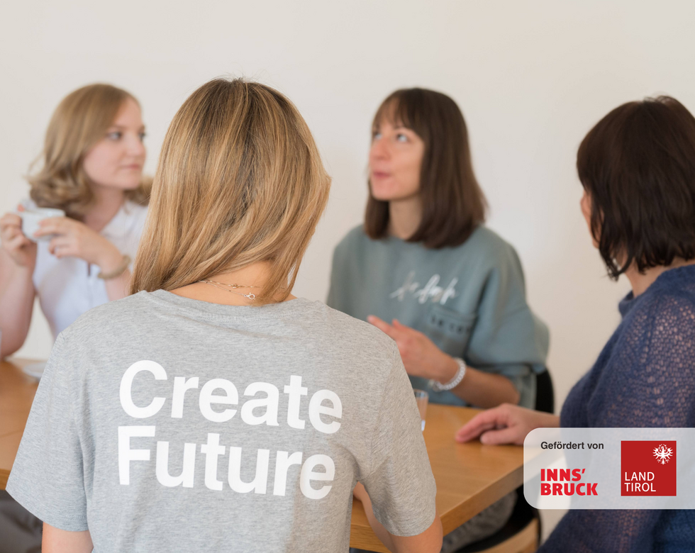 Foto von sitzenden Personen um Tisch herum, Create Future Aufschrift auf einem Shirt sichtbar