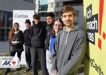 Fünf junge Menschen stehen vor einem Gebäude neben einem „ich mach was“-Schild.