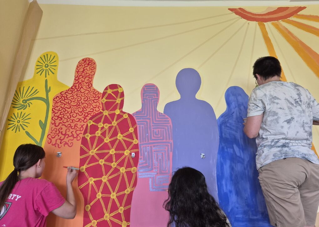 Foto von drei malenden Perosnen, die lebensgroße Menschenformen in bunten Farben an Wand malen