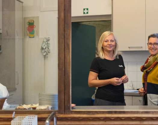 Zwei Frauen lächeln und stehen in einer hellen, modernen Küche, umgeben von Kochutensilien und einem einladenden Ambiente.