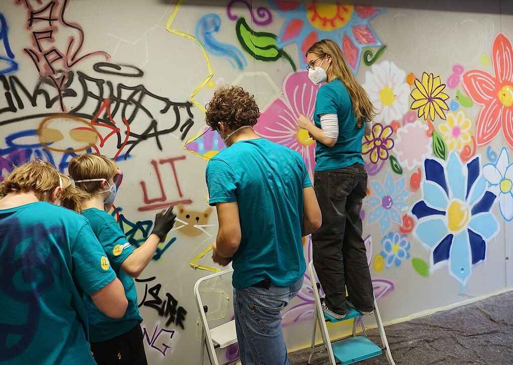Jugendliche auf Leitern stehend, die eine Hauswand mit Graffiti besprayen