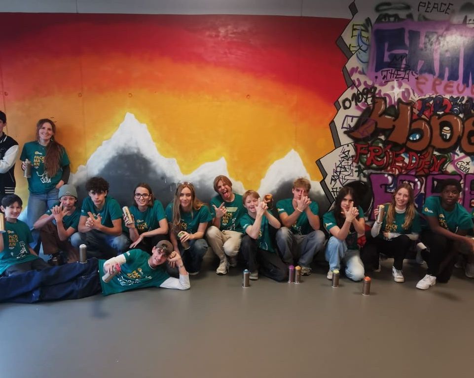 Eine lebendige Jugendgruppe posiert vor einem Graffiti-Hintergrund, lächelt und hält Spraydosen in der Hand.
