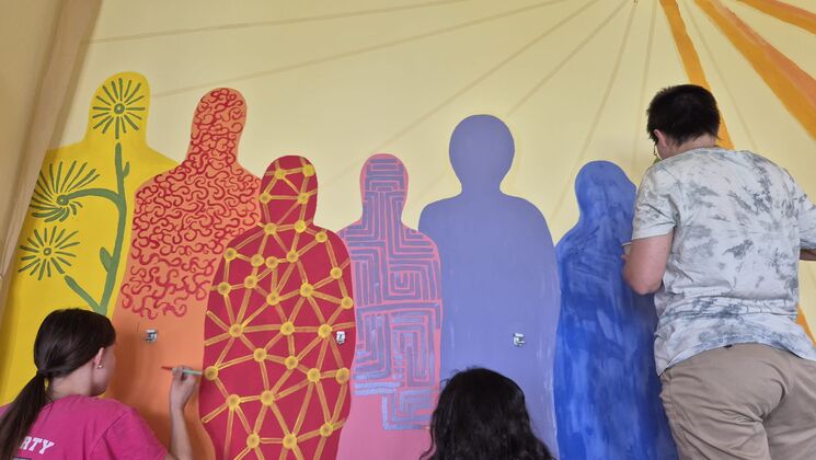 Foto von drei malenden Perosnen, die lebensgroße Menschenformen in bunten Farben an Wand malen